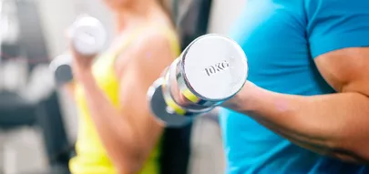 Ein Mann und eine Frau halten Hanteln in einem Fitnessstudio.