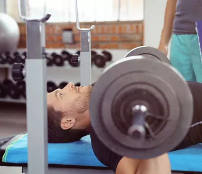 Mann trainiert Bankdrücken wird von Fitnesstrainer mit Schreibblock betreut