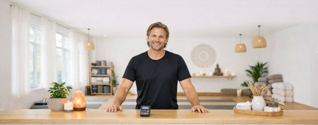 ein Yoga Nidra Trainer steht hinter dem Tresen eines Yoga Studios und lächelt in die Kamera