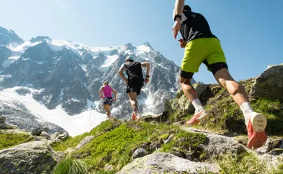 drei Trailrunner, zwei Männer und eine Frau, laufen an einem heißen, hellen Sommertag einen steilen Pfad in den Bergen der Alpen hinauf