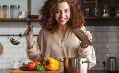 Frau hält einen Kochlöffel beim kochen einer Suppe in der Küche