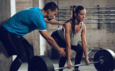 Frau trainiert mit sehr schwerer Langhantel mit Personal Trainer