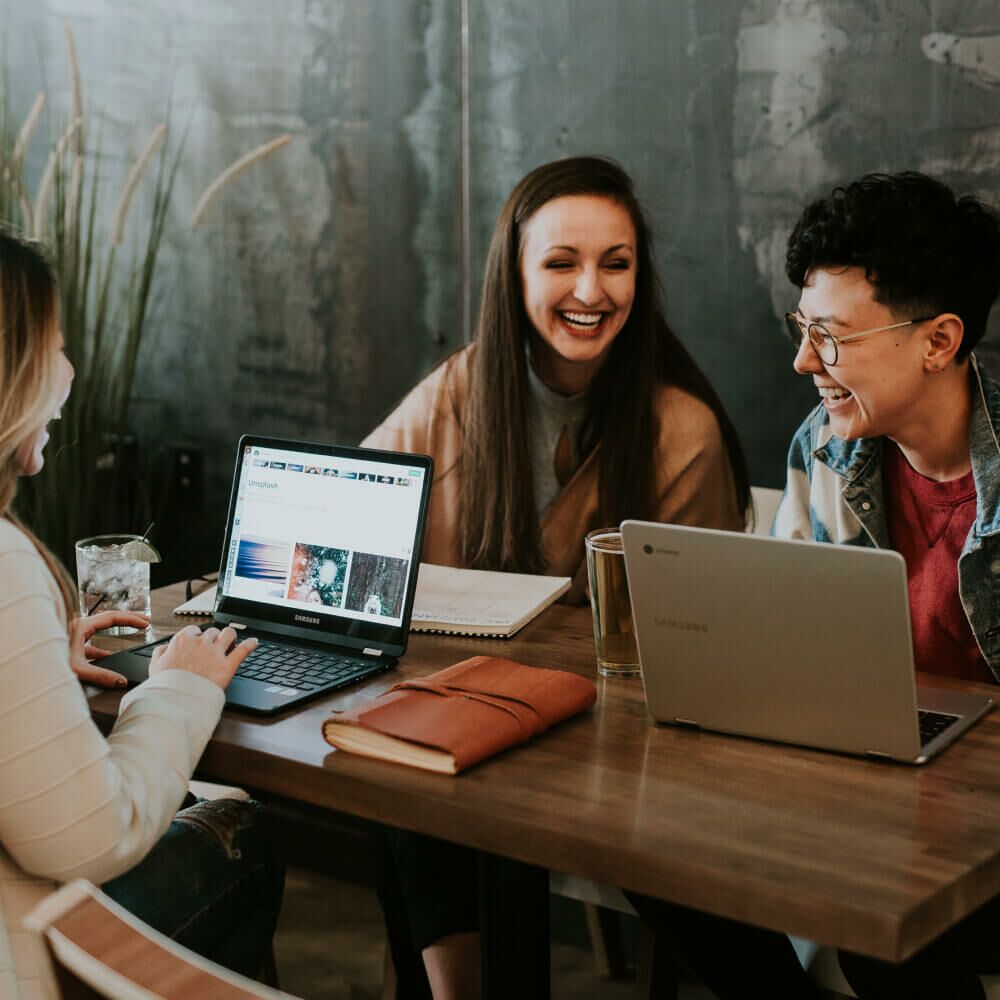 Drei Frauen sitzen mit Laptops an einem Tisch.